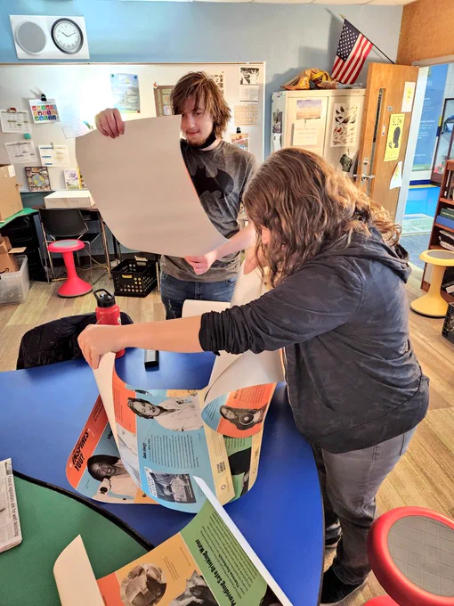A student and adult checking out a stack of posters