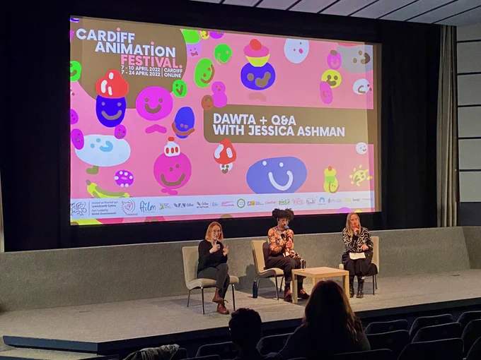 A photograph of three people sitting on stage inside a cinema screening room. All three of them are holding microphones and facing the audience. Behind them is a screen that shows the CAF poster, along with the text: Dawta   Q&A with Jessica Ashman.