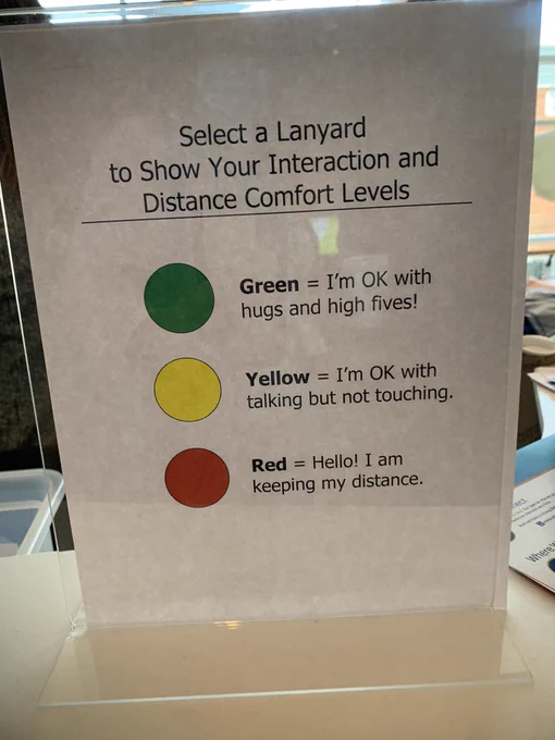 Sign with instructions on how to choose a lanyard that says Green = I’m ok with hugs and high fives! Yellow = I’m okay with talking but not touching. Red = Hello! I’m keeping my distance.