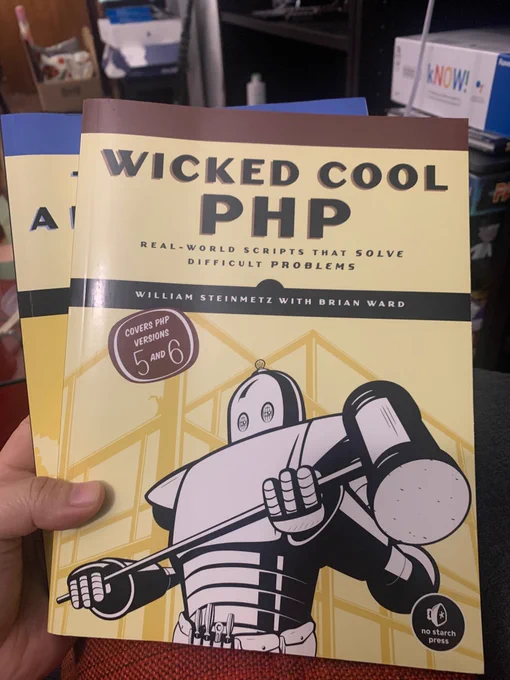A yellow book with title Wicked Cool PHP, it has a picture of a white robot holding a hammer shaped tool. It has a brown oval with  white text that says “Cover PHP version 5 and 6”