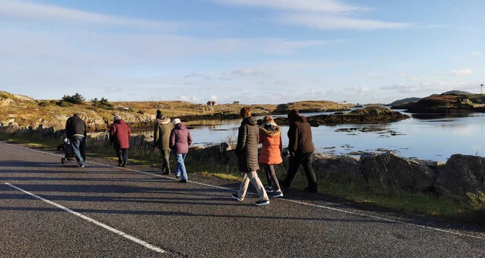 A group of walkers on a road on North Bay in the Isle of Barra with a rocky sea loch to the right of them.