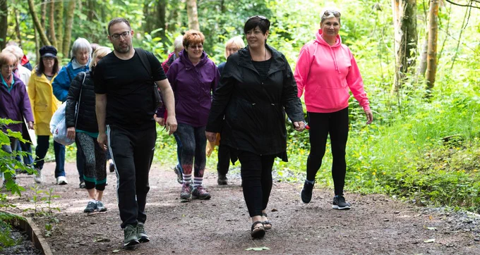 Large group of walkers on a wide accessible path in the woods.