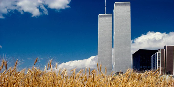 Photo of an environmental artwork by Agnes Denes; a wheatfield in the foreground and World Trade Center buildings in the background against a clouded blue sky.