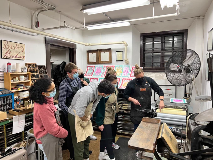 Students watch a presentation on using a printing press.