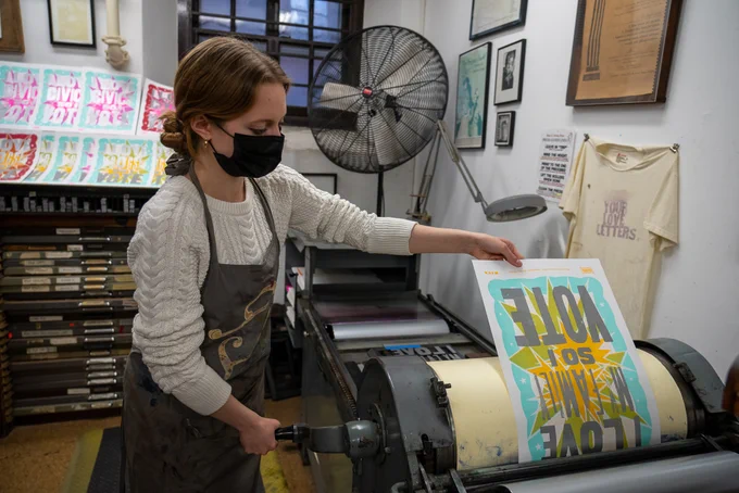 An IOP student makes a poster using a printing press.