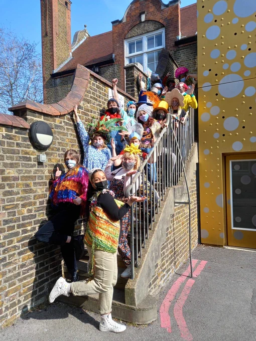 A group of people wearing colourful costumes, hats and jackets wearing face coverings. The group are standing on a brick staircase all in different poses and positions.