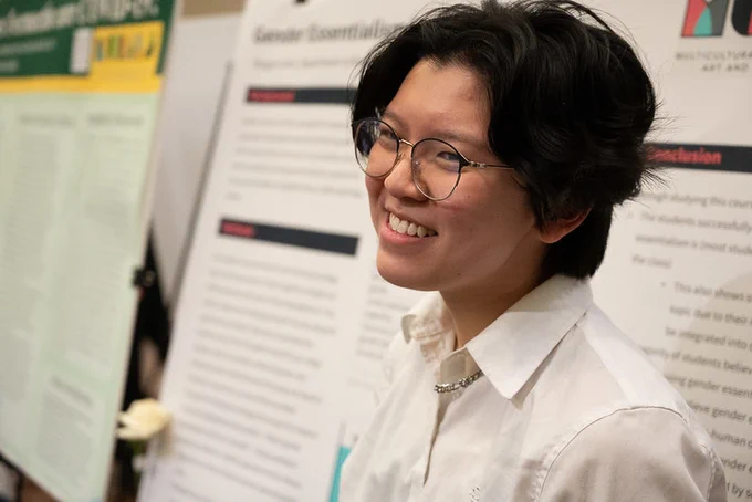 A student smiles in front of a poster board presentation.