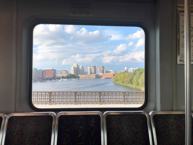 Image credit: Rubén Morgan, image of the Boston/Cambridge Skyline   Museum of Science through a window taken from inside a Red Line car passing over the Charles River. Seats can be seen in the foreground, while the background shows the Charles River and city scape.