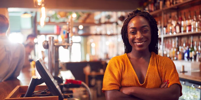 Female pub manager standing behind the bar smiling with arms crossed