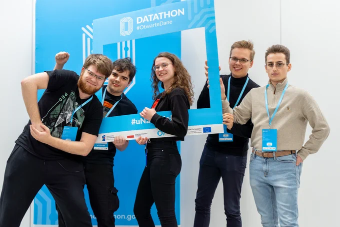 Na zdjęciu pięć osób, uczestnicy Datathonu #OtwarteDane, trzymający w dłoniach dużą ramkę do zdjęć z logotypem Datathon #OtwarteDane oraz logotypami Fundusze Europejskie; RP; Projekt otwarte dane plus; UE
