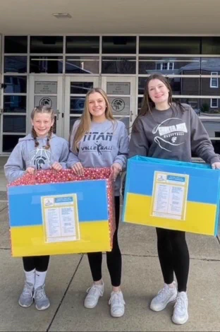 three students holding collection boxes decorated with Ukrainian flag