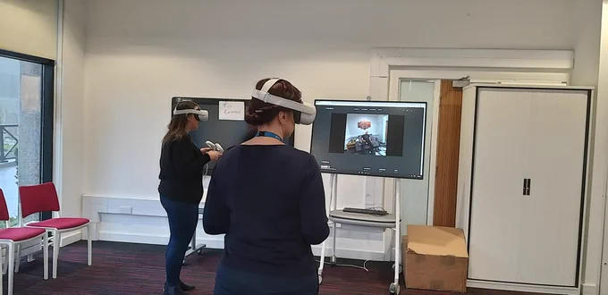 Two women wearing virtual reality headsets, with one casting what they are seeing to a screen