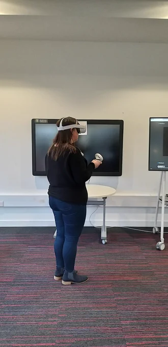 A woman facing away from the camera wearing a virtual reality headset with hand held controllers