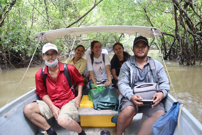 Two men and three women sit in a boat on a river on the way to visit a research site in Cambodia