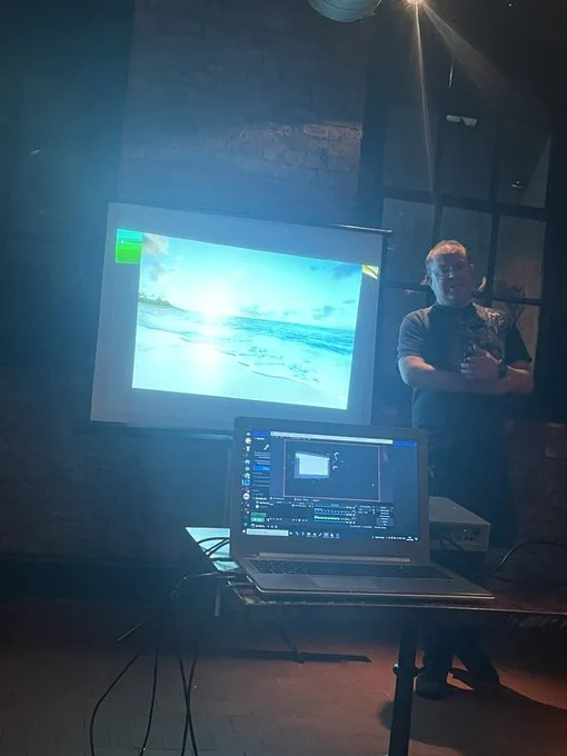 Andrew Waite, presenting on AWS Security topics at DC44191 event. Screen shows a slide with photo of a sunny beach.