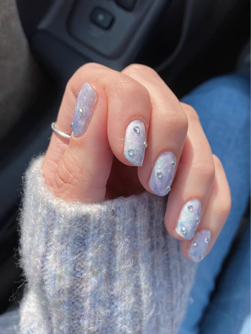 Hand painted pastel marbled pink, white, baby blue and lavender nail design with three gemstones on each nail on a left hand in a fist position
