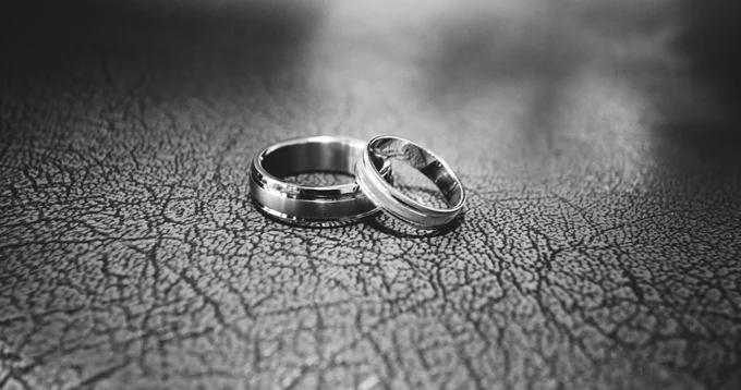 A pair of wedding rings on a tabletop, one leaning on the other.