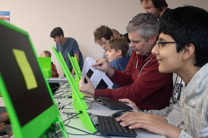 Teenage boy coding on a pitop Raspberry Pi with a parent in the background doing the same.