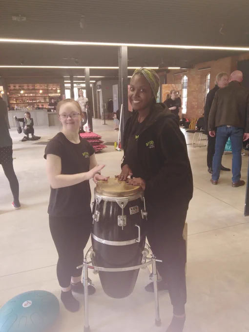Anna - Hubbub Actor and Lauren - Hubbub Facilitator standing with a conga drum in The Museum of Making Derby. They are both smiling at the camera. 
