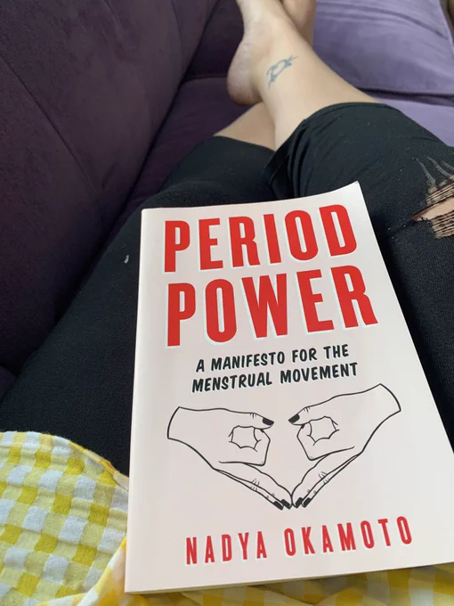 Lap on a purple couch with pink book “Period Power: A Manifesto for the Menstrual Movement” by Nadya Okamoto