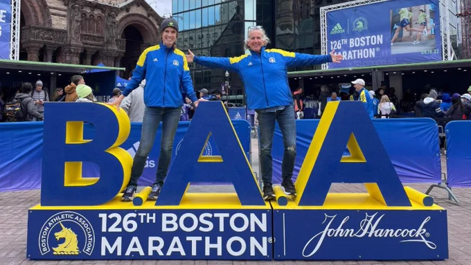 Boston Marathoners Jennifer Govostis and Mel Latt standing on the BAA sign.