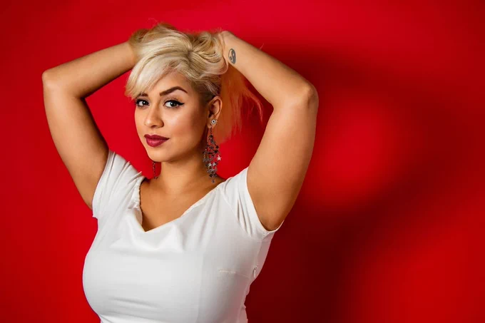 Rush Kazi poses with their hands above their hand against a deep red backdrop.