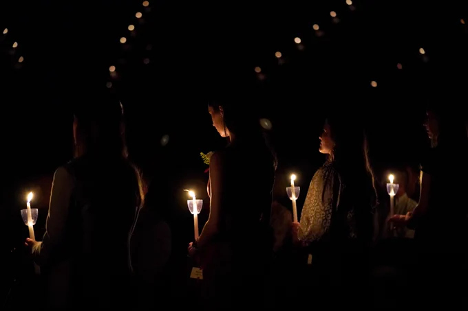A line of people holding candles from behind in a dark reed arena