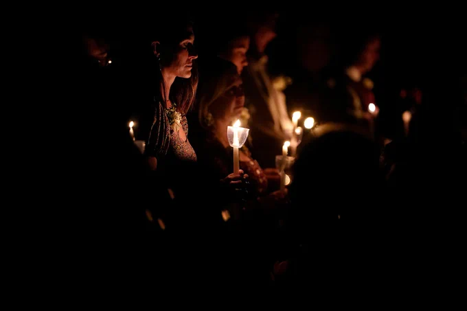 A line of people holding candles with their eyes closed