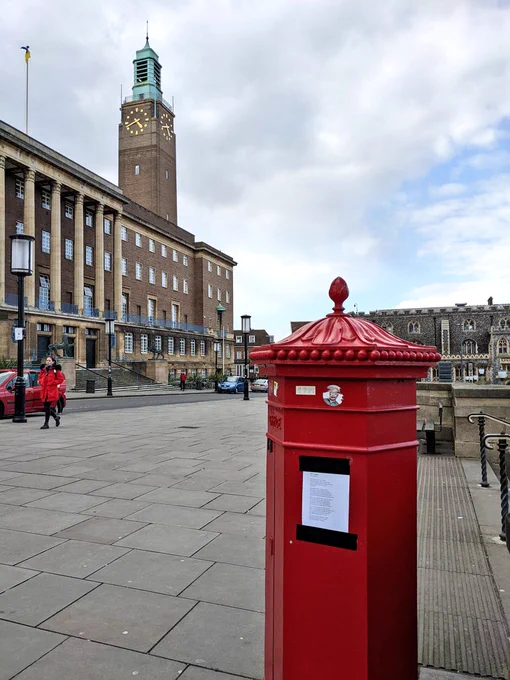 A book page duct taped to a bright red postbox in a city centre.