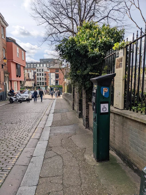 A book page taped to a parking meter on a city side street. The page features an artwork of words forming a ring. At the top of the ring, the words expand out as if two points collided.