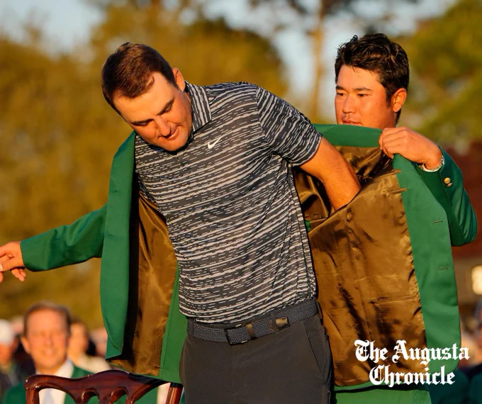 Hideki Matsuyama putting the green jacket on Scottie Scheffler.