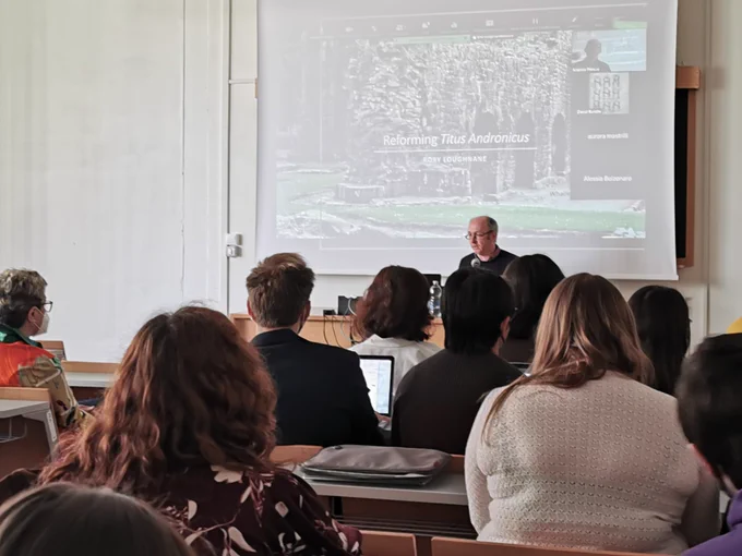 Rory sitting at the desk facing the room, giving his talk, with a PowerPoint behind him.