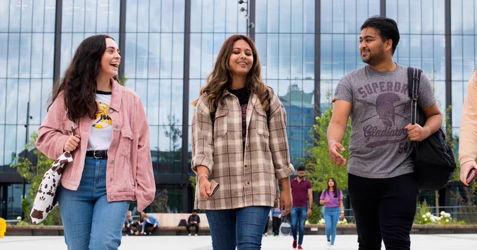 Photo of three students chatting and walking across our University Square