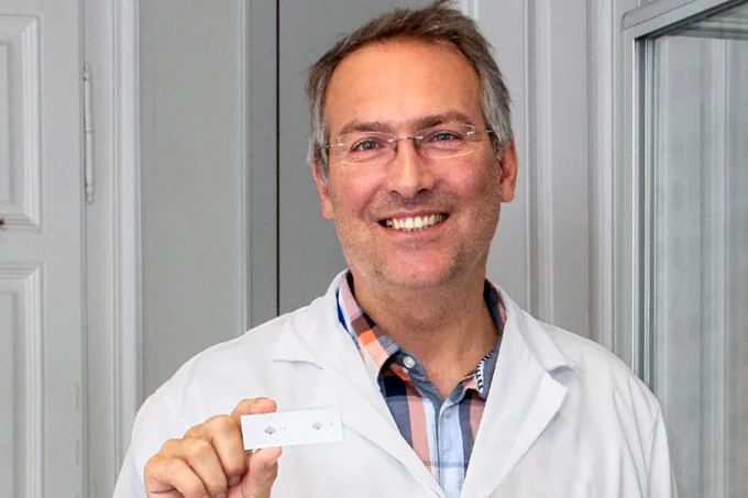 Peterl Ertl hält einen Biochip in die Kamera und lächelt. 