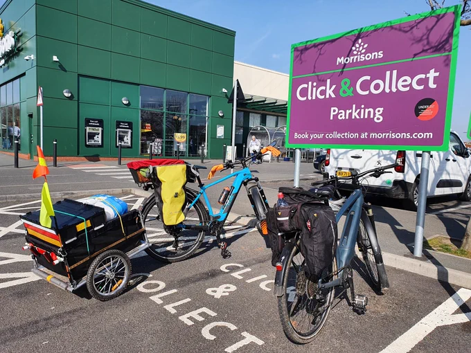 Two cycles with shopping in panniers and trailer at Click & Collect supermarket parking