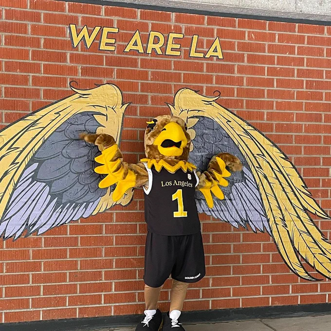 eddie the eagle posing in front of eagle wings painted on a brick wall