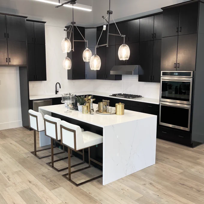 Image of kitchen setup with white island, white bar stools, and black cabinets.