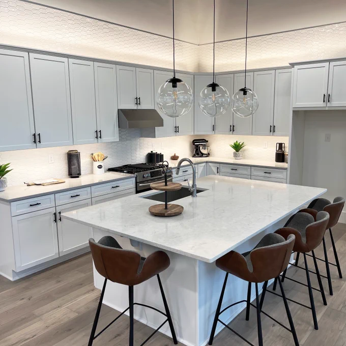 Image of white kitchen with white countertops, brown bar stools, and white cabinets.