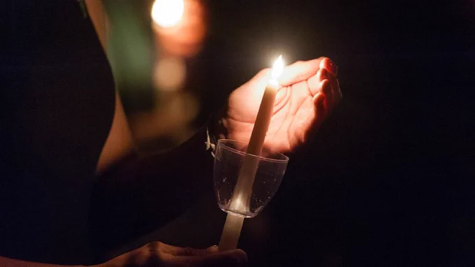 A person holding a candle and shielding the light with their hand in the dark at a Muster ceremony