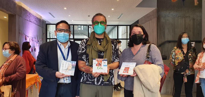 Tres personas muestran cada uno de los ejemplares de los libros lanzados hoy, los sostienen en sus manos. Las tres personas están al interior de un edificio y usan mascarillas. 