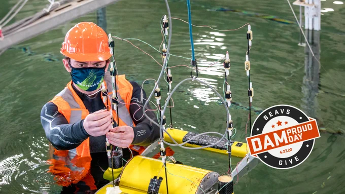Student stands in the large wave basin of the O.H. Hinsdale Wave Research lab working on a device as part of a marine energy challenge.
