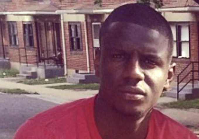 An image of Freddie Gray, from the shoulders up, wearing a red t-shirt and looking directly into the camera.