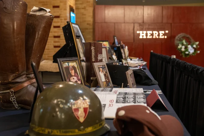 Memorial at the Reflections Display includes corps boots, a corps helmet, and a maroon Baseball cap. It also includes a yearbook and framed photos of the honored individual. 