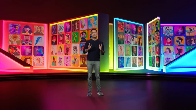 A photo of a man standing on a stage in front of multi-colored, lit panels. The panels have smaller, square images of different pieces of artwork.