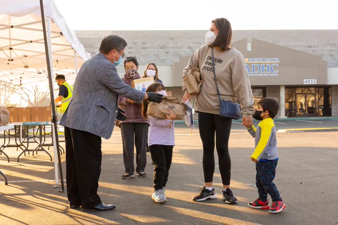 A volunteer hands a mother and her kids a Pass the Love meal kit at a distribution site. 
