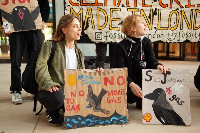 In bright photos people crouch in from of a banner with reads, in yellow and orange 'Climate Crisis Made in London', they hold placards reading 'Stop Jackdaw' with hand painted birds on them