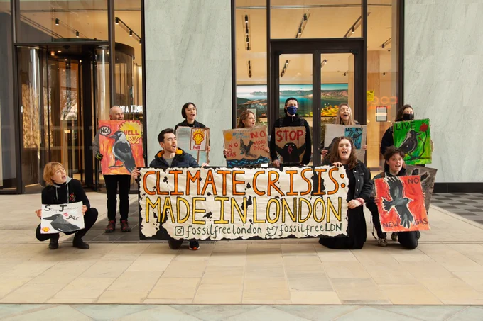 A group stands in front of the glass doors of Shell's London HQ with banner and placards