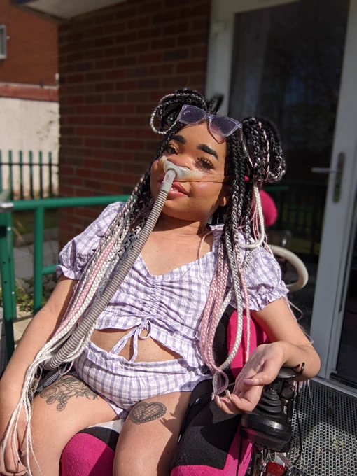 Shelby posing in the sunshine wearing a checkered purple crop top with matching shorts and purple sunglasses 