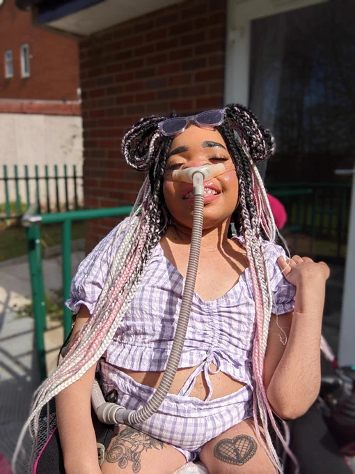 Shelby posing in the sunshine wearing a checkered purple crop top with matching shorts and purple sunglasses 