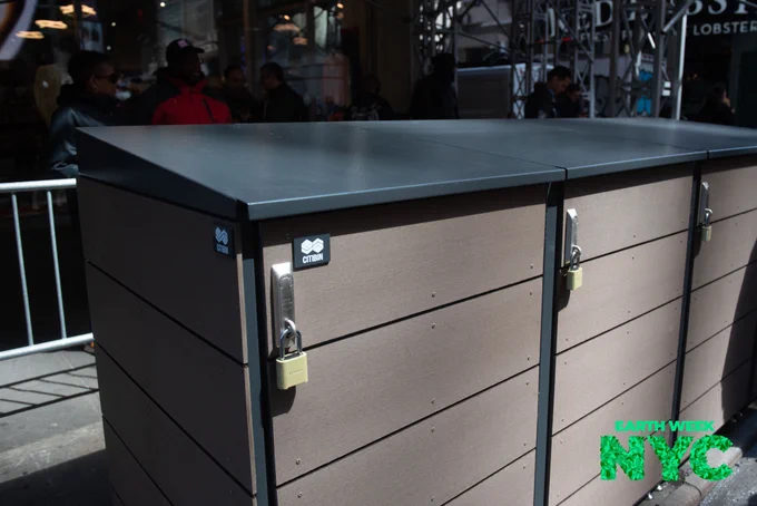 A photo of a large container for trash that has four individual doors on the front of it, each with a small padlock.